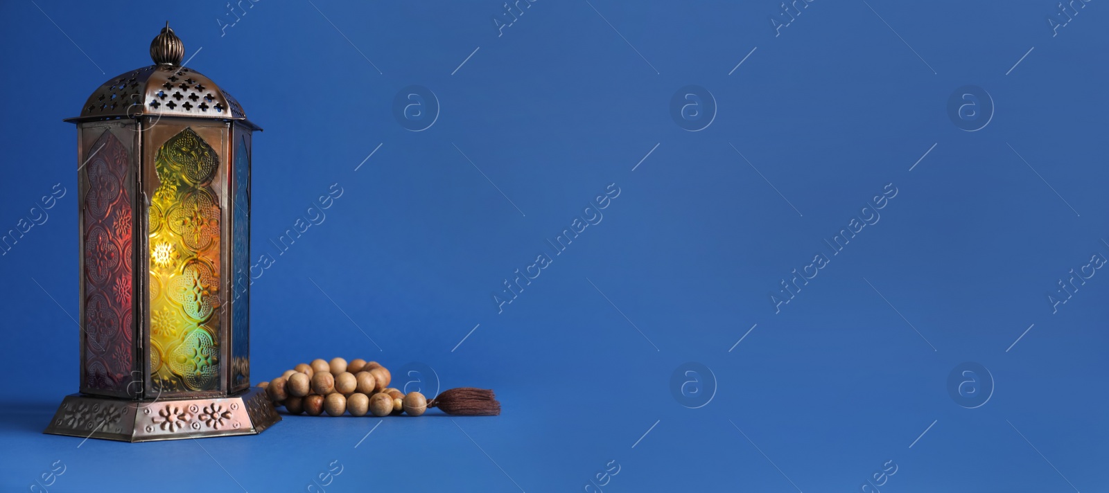 Photo of Decorative Arabic lantern and prayer beads on blue background. Space for text