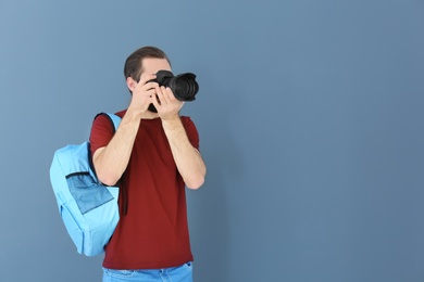 Young photographer with professional camera on color background