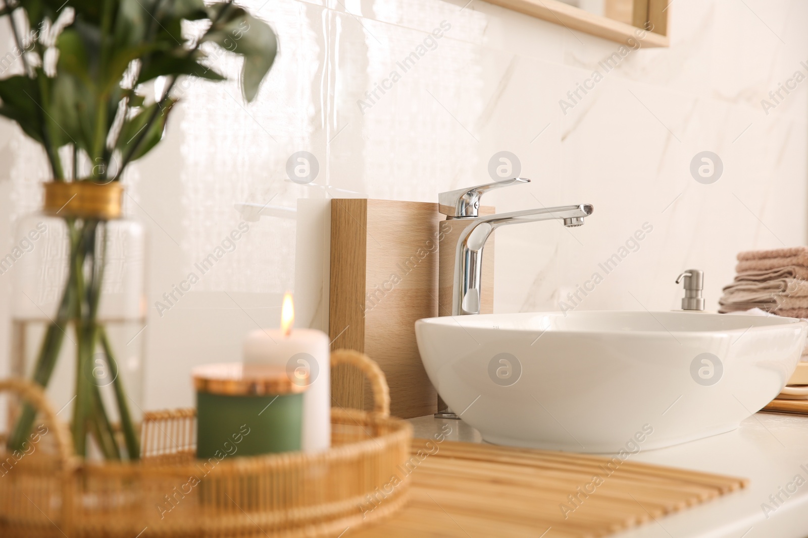 Photo of Vase with beautiful branches, candles and fresh towels near vessel sink in bathroom. Interior design