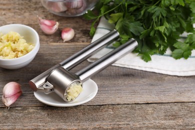 Photo of Garlic press, cloves and mince on wooden table. Kitchen utensil