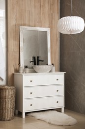 Photo of Chest of drawers with sink, mirror and toiletries in bathroom. Interior design