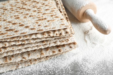 Photo of Stack of traditional matzos, rolling pin and flour on table, closeup