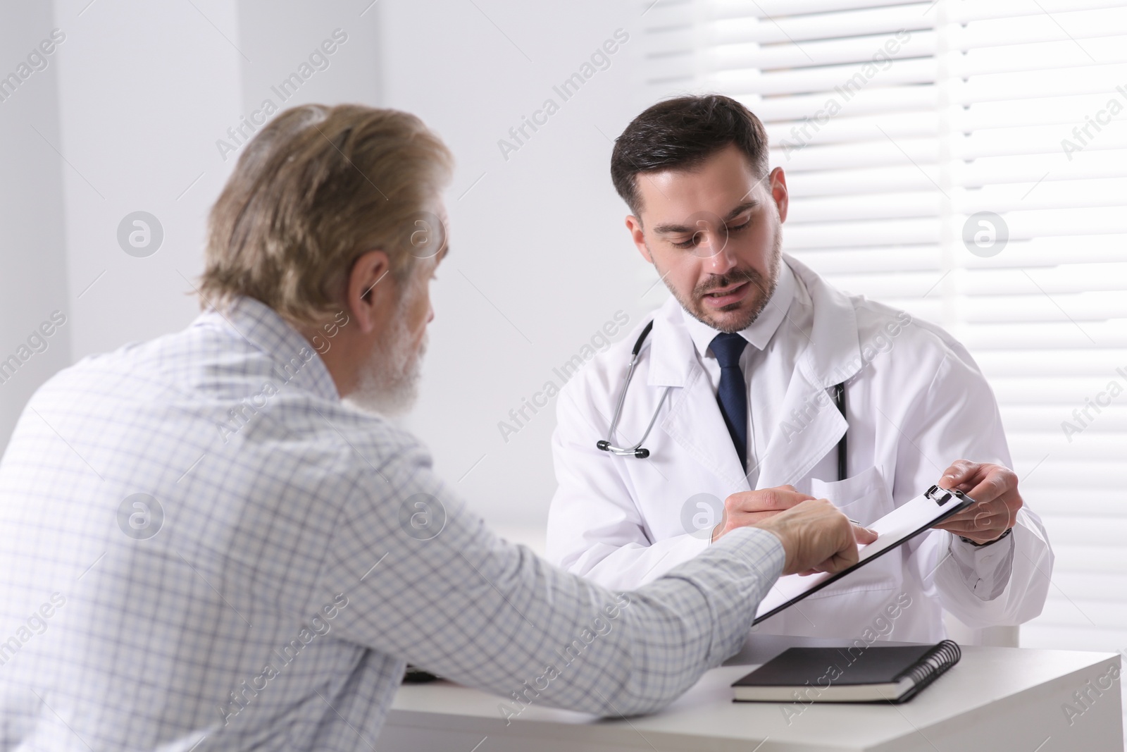 Photo of Doctor consulting senior patient at white table in clinic