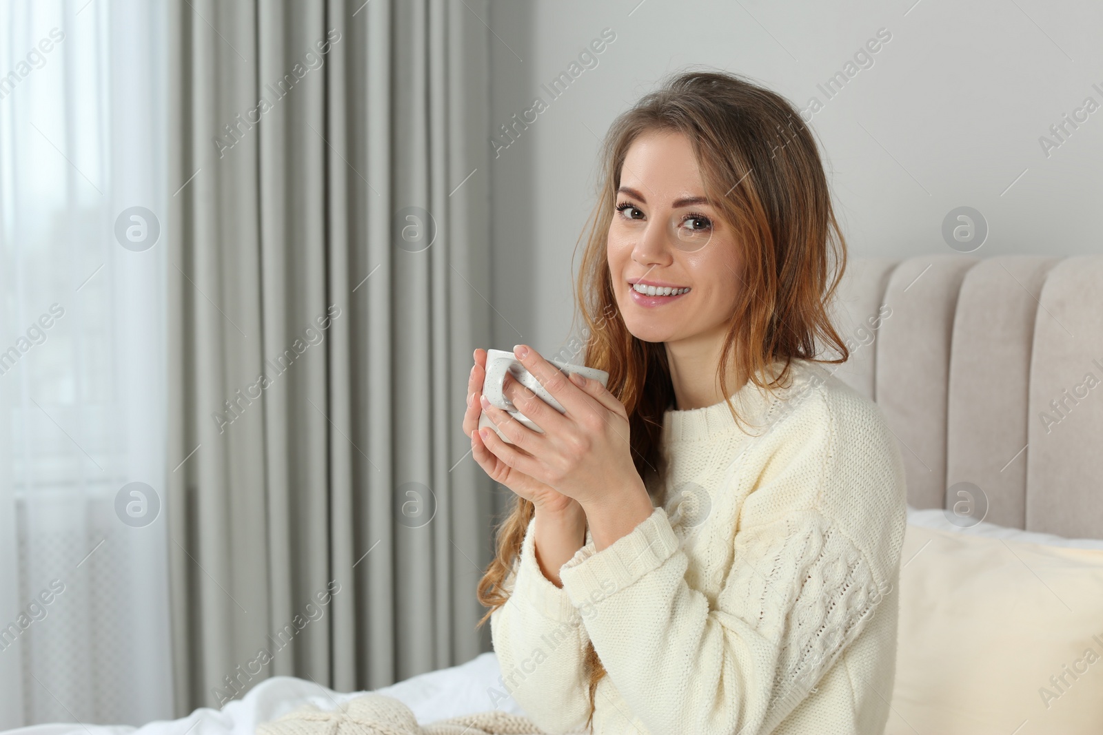 Photo of Happy beautiful woman with cup of drink in bed at home