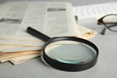 Photo of Magnifying glass and stack of newspapers on grey table, closeup. Job search concept
