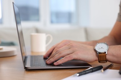 Photo of Man working on laptop at wooden desk indoors, closeup