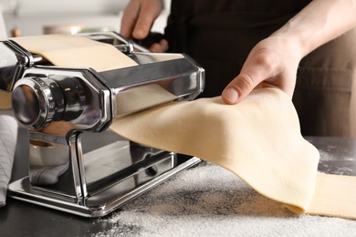 Photo of Young man preparing noodles on pasta maker at table