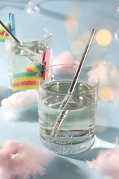 Tasty cocktails in glasses decorated with gummy candies and cotton candy on light blue background