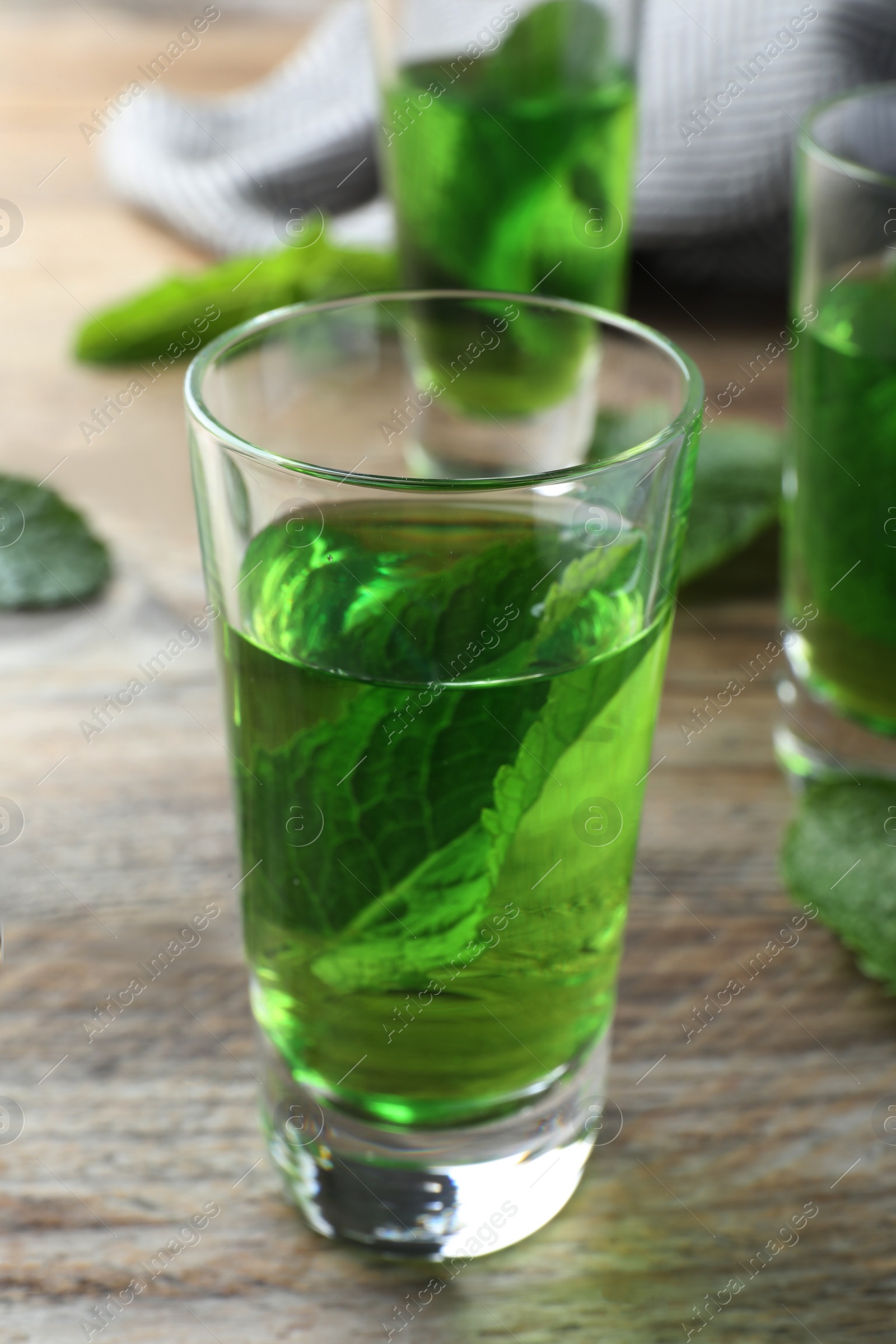 Photo of Delicious mint liqueur with green leaves on wooden table, closeup