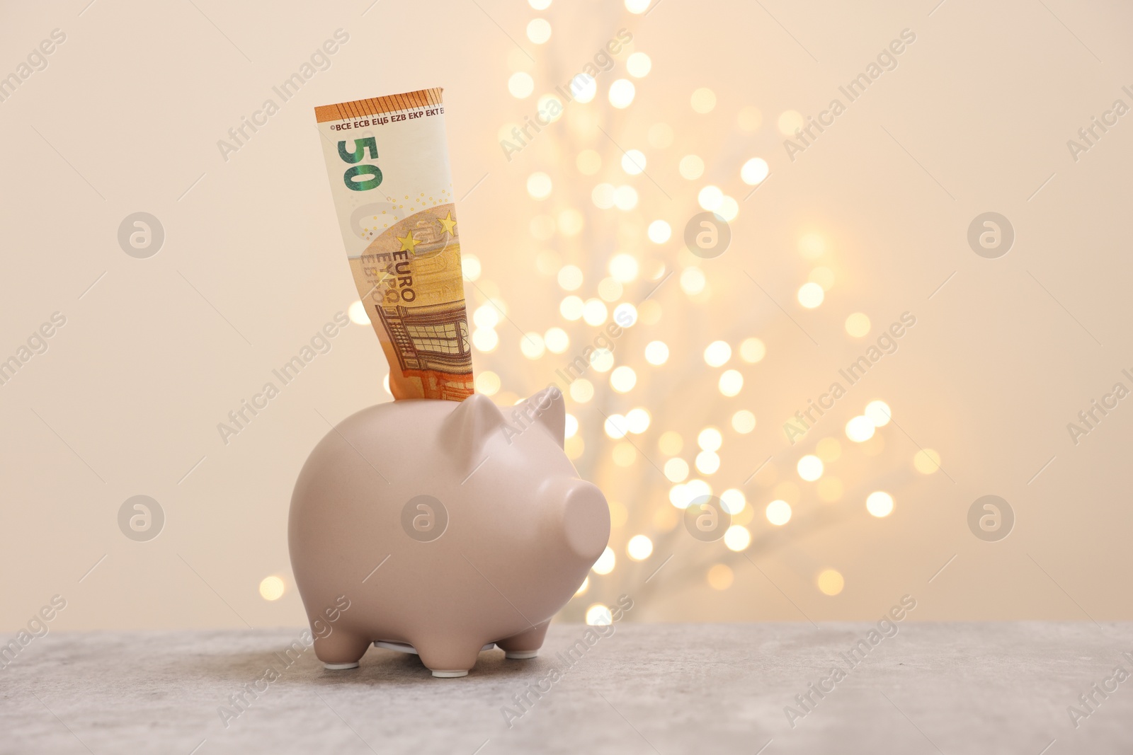 Photo of Piggy bank with euro banknote on grey table against blurred lights, space for text