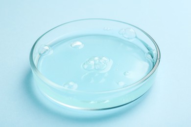 Photo of Petri dish with liquid sample on light blue background, closeup
