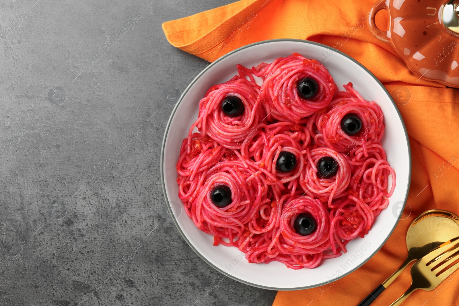 Photo of Red pasta with olives in bowl on grey textured table, flat lay with space for text. Halloween food