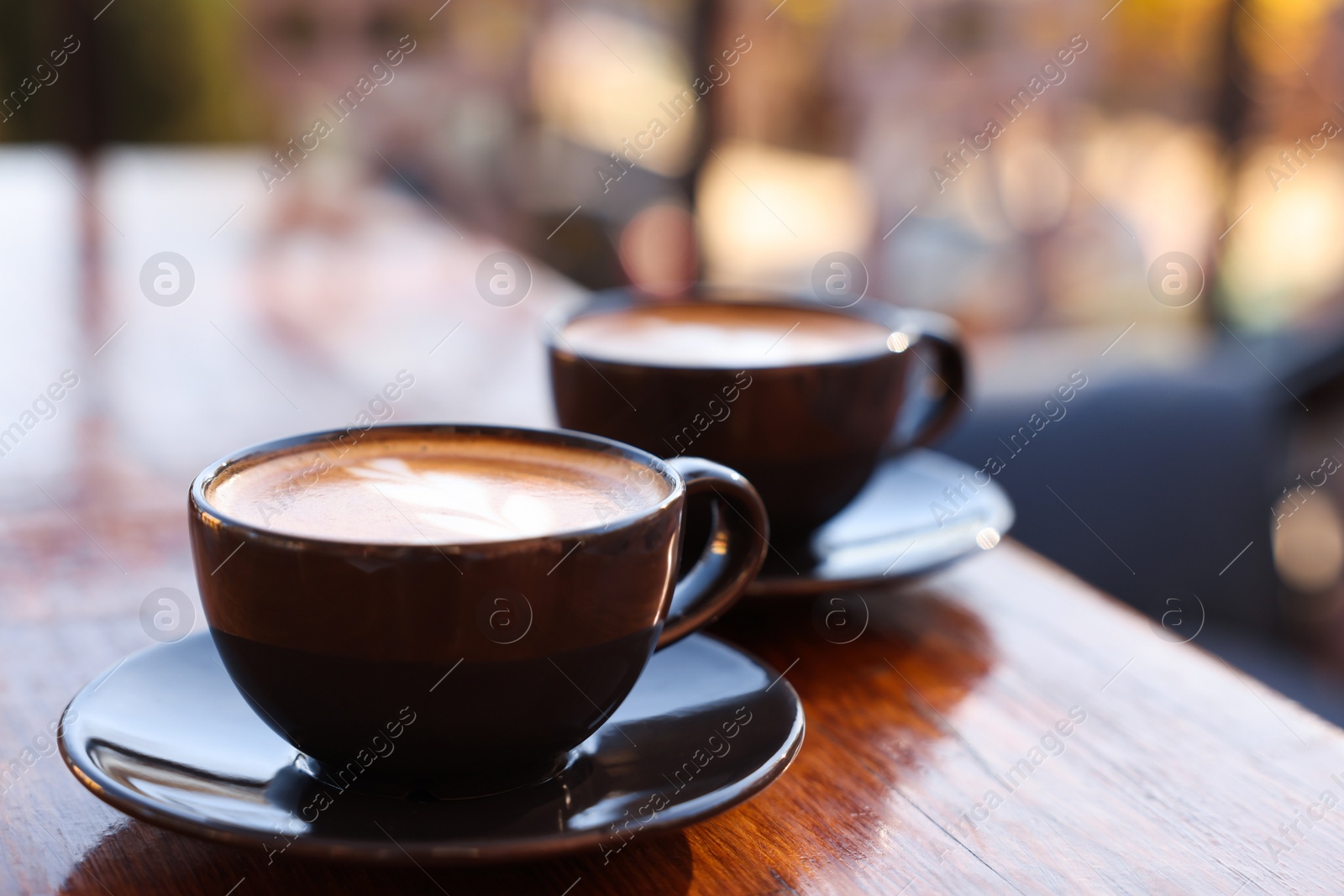 Photo of Cups of aromatic coffee with foam on wooden table in outdoor cafe. Space for text