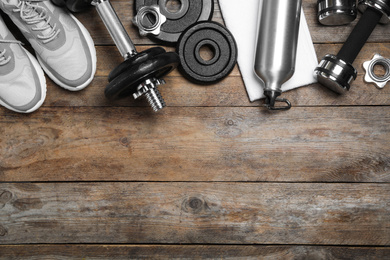 Photo of Gym equipment and shoes on wooden background, flat lay. Space for text