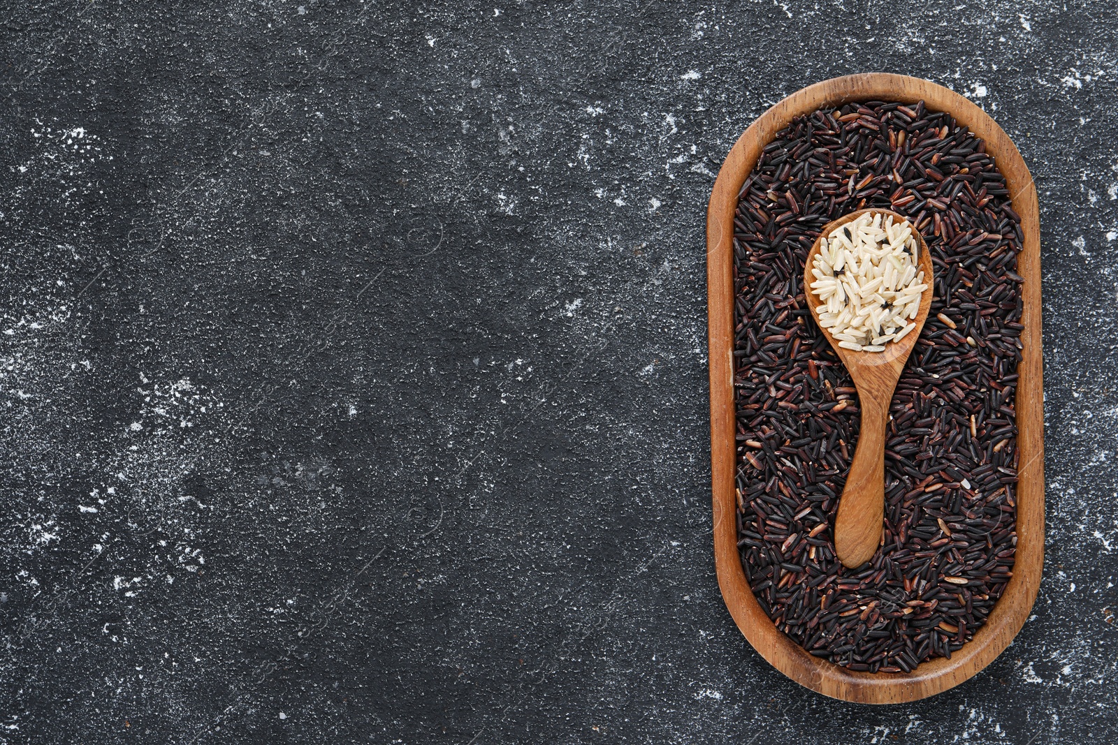 Photo of Spoon and dish with different sorts of rice on black textured table, top view. Space for text