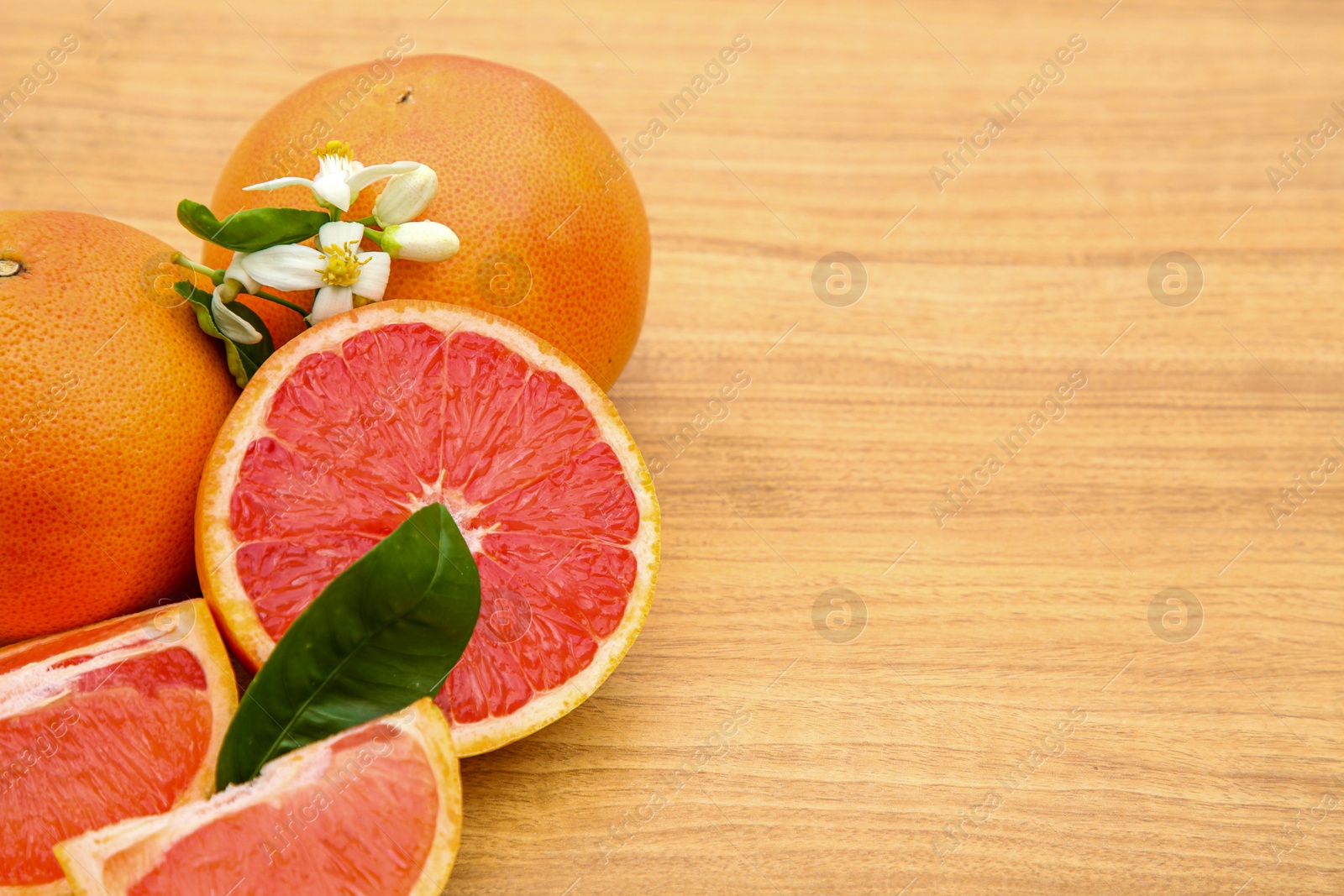 Photo of Fresh ripe grapefruits, flowers and green leaves on wooden table. Space for text