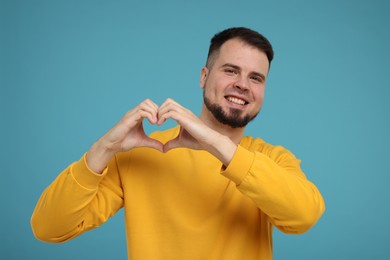 Photo of Man showing heart gesture with hands on light blue background