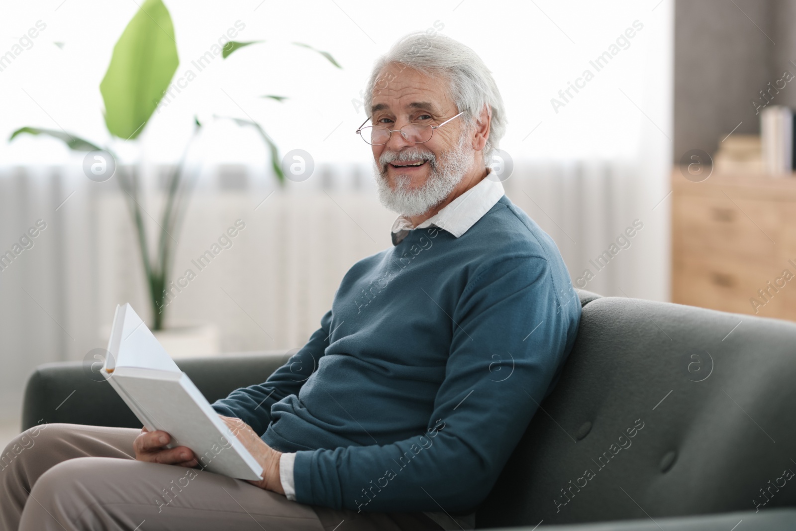 Photo of Portrait of happy grandpa reading book on sofa indoors