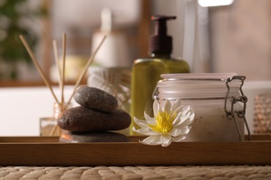 Photo of Different spa products and beautiful flower on wicker table in bathroom, closeup