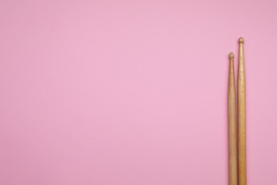 Two wooden drum sticks on pink background, top view. Space for text