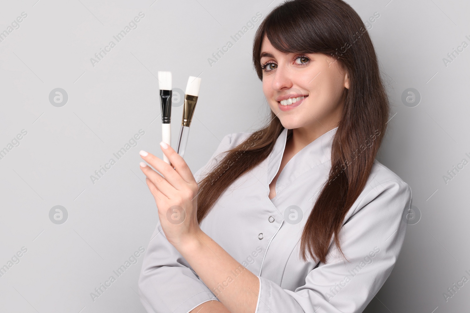 Photo of Cosmetologist with cosmetic brushes on grey background