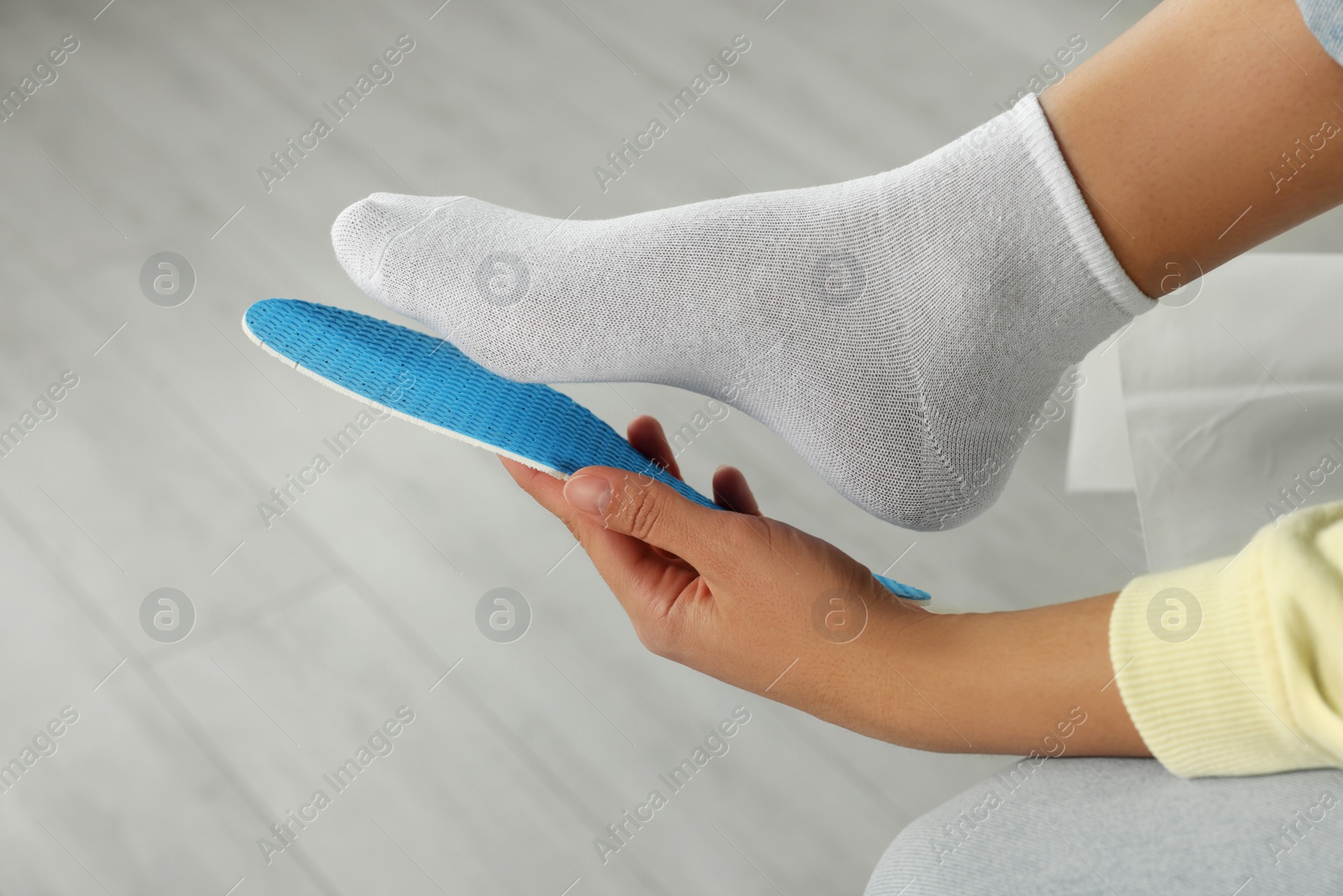 Photo of Woman fitting orthopedic insole to her foot indoors, closeup