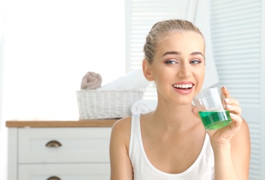 Photo of Woman holding glass with mouthwash in bathroom. Teeth care