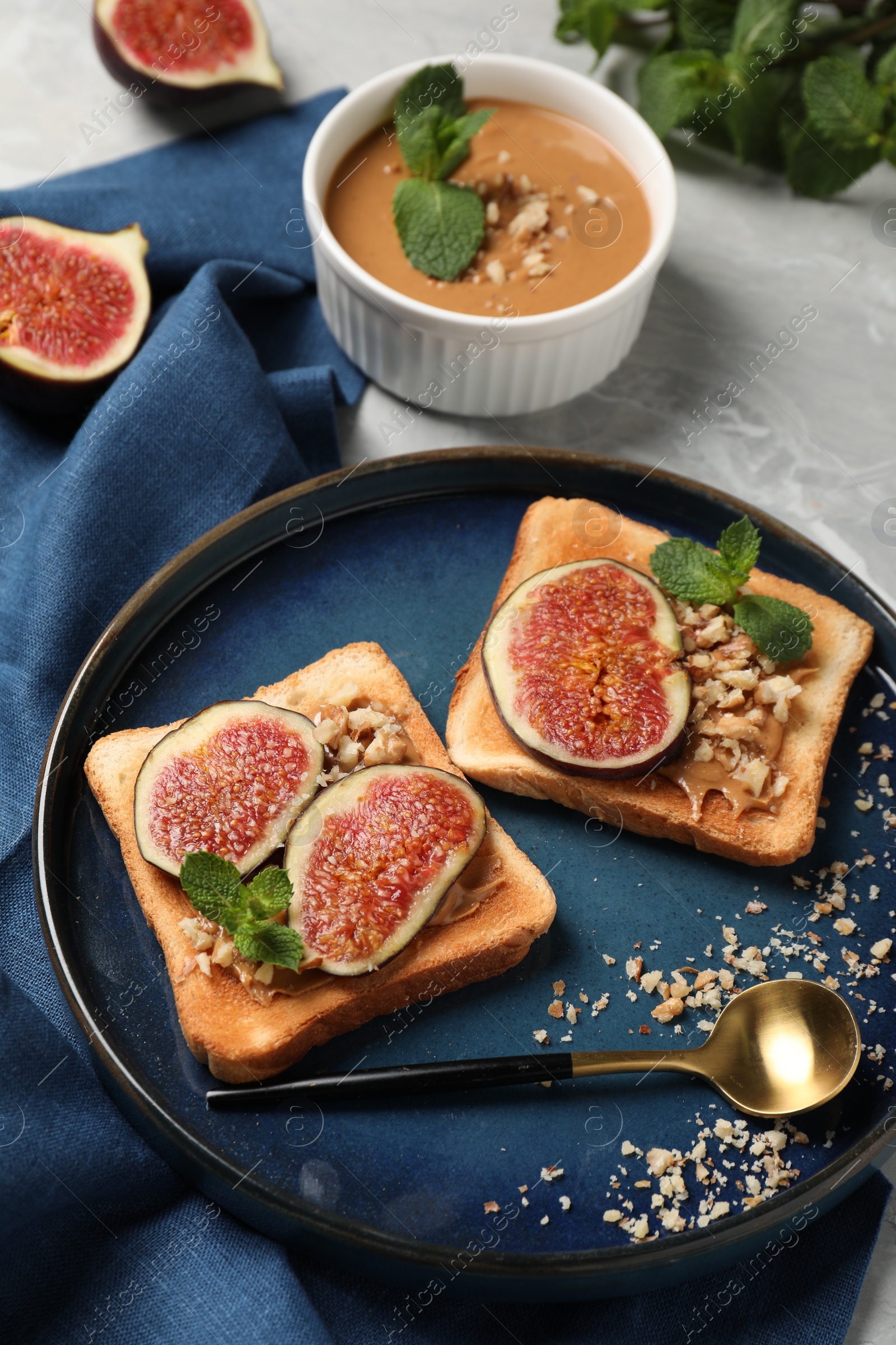 Photo of Tasty toasts served with fig, peanut butter and walnuts on light grey marble table, above view