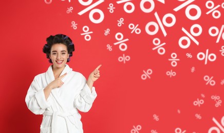 Discount offer. Happy woman in bathrobe with hair curlers pointing at falling percent signs on red background, banner design