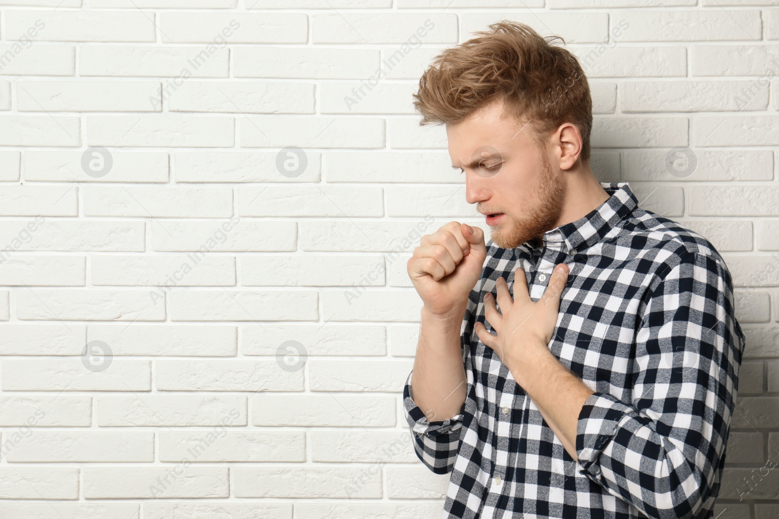 Photo of Handsome young man coughing near brick wall. Space for text