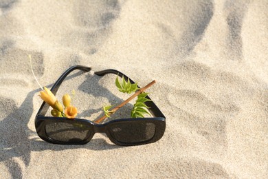 Photo of Stylish sunglasses and tropical flower on sand, space for text