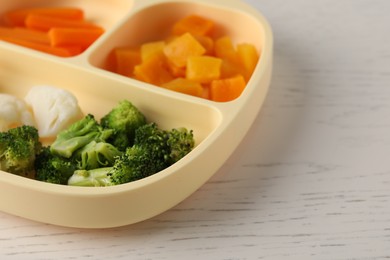 Photo of Baby food. Section plate with different vegetables on white wooden table, closeup. Space for text