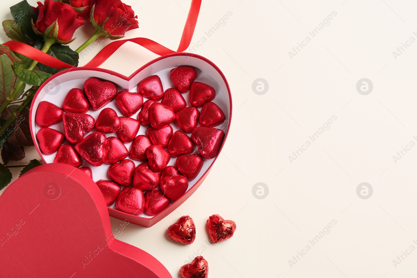 Photo of Heart shaped chocolate candies and bouquet on beige background, flat lay