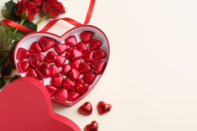 Heart shaped chocolate candies and bouquet on beige background, flat lay