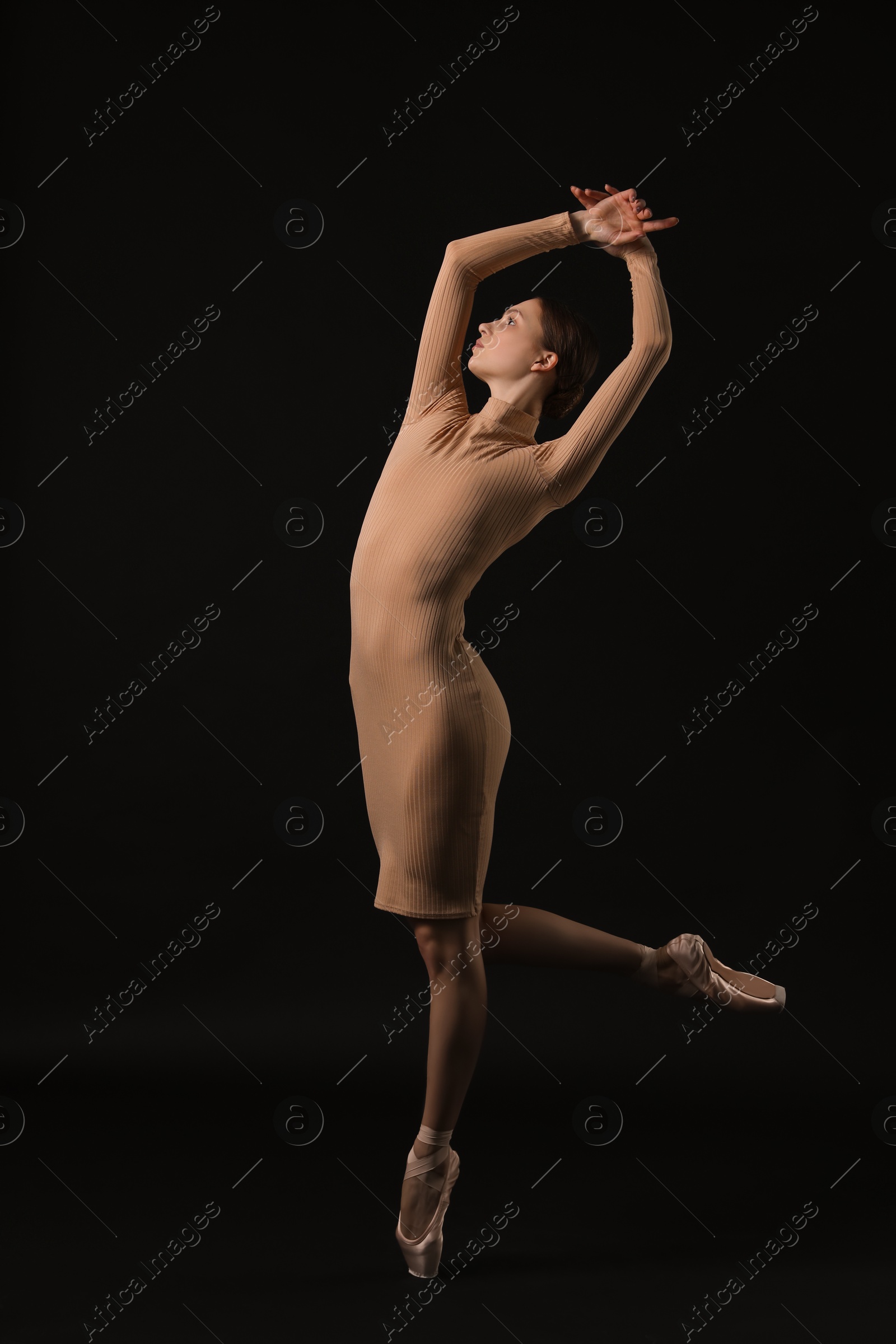 Photo of Young ballerina in pointe shoes dancing on black background