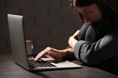 Photo of Woman using laptop at table against in dark room. Loneliness concept