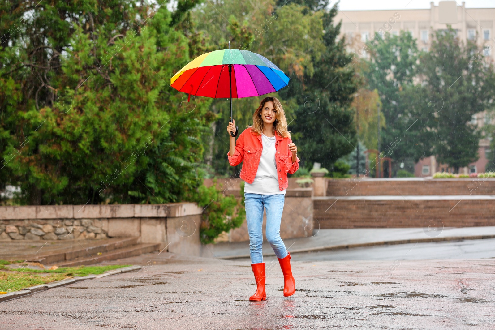 Photo of Happy young woman with bright umbrella under rain outdoors