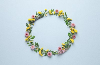 Photo of Wreath made of beautiful flowers and green leaves on light blue background, flat lay. Space for text