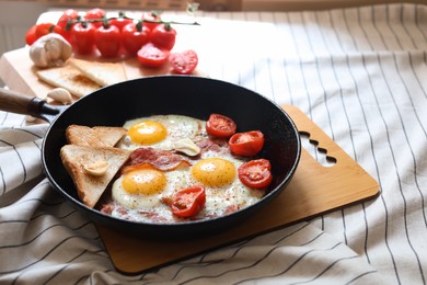 Photo of Delicious fried eggs with bacon and tomatoes in pan on table