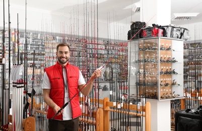 Photo of Salesman with fishing rod in sports shop. Space for text