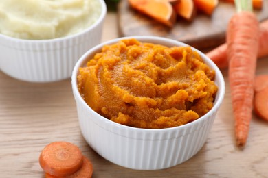 Photo of Bowl with tasty carrot puree and ingredients on wooden table, closeup