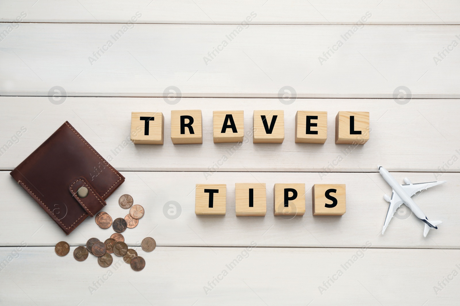 Photo of Phrase Travel Tips made with cubes, coins and toy plane on white wooden table, flat lay