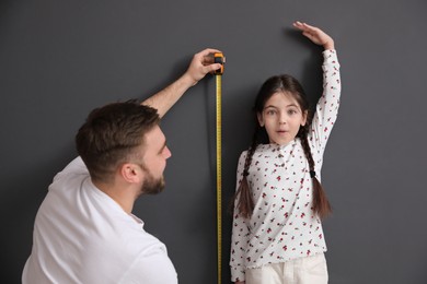 Photo of Father measuring daughter's height near black wall