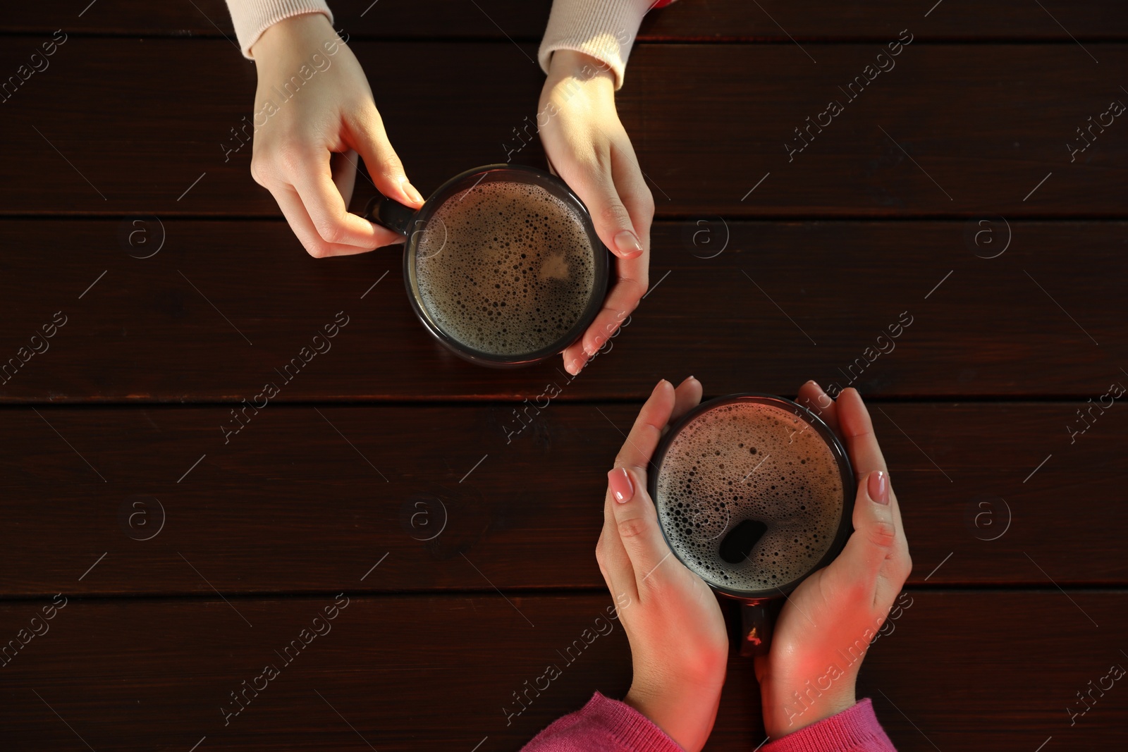 Photo of Women with cups of hot coffee at wooden table, top view