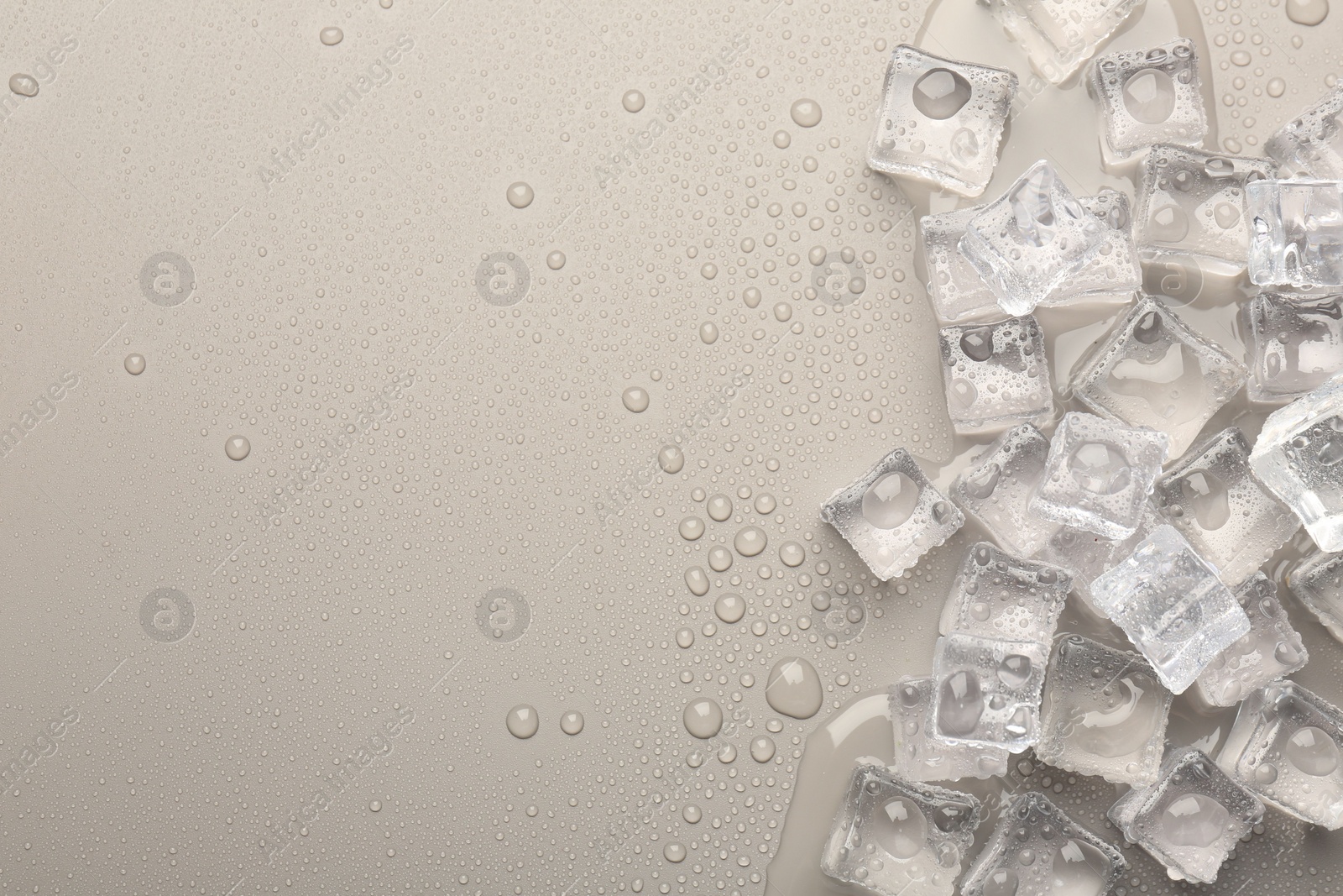 Photo of Melting ice cubes and water drops on light grey background, flat lay. Space for text