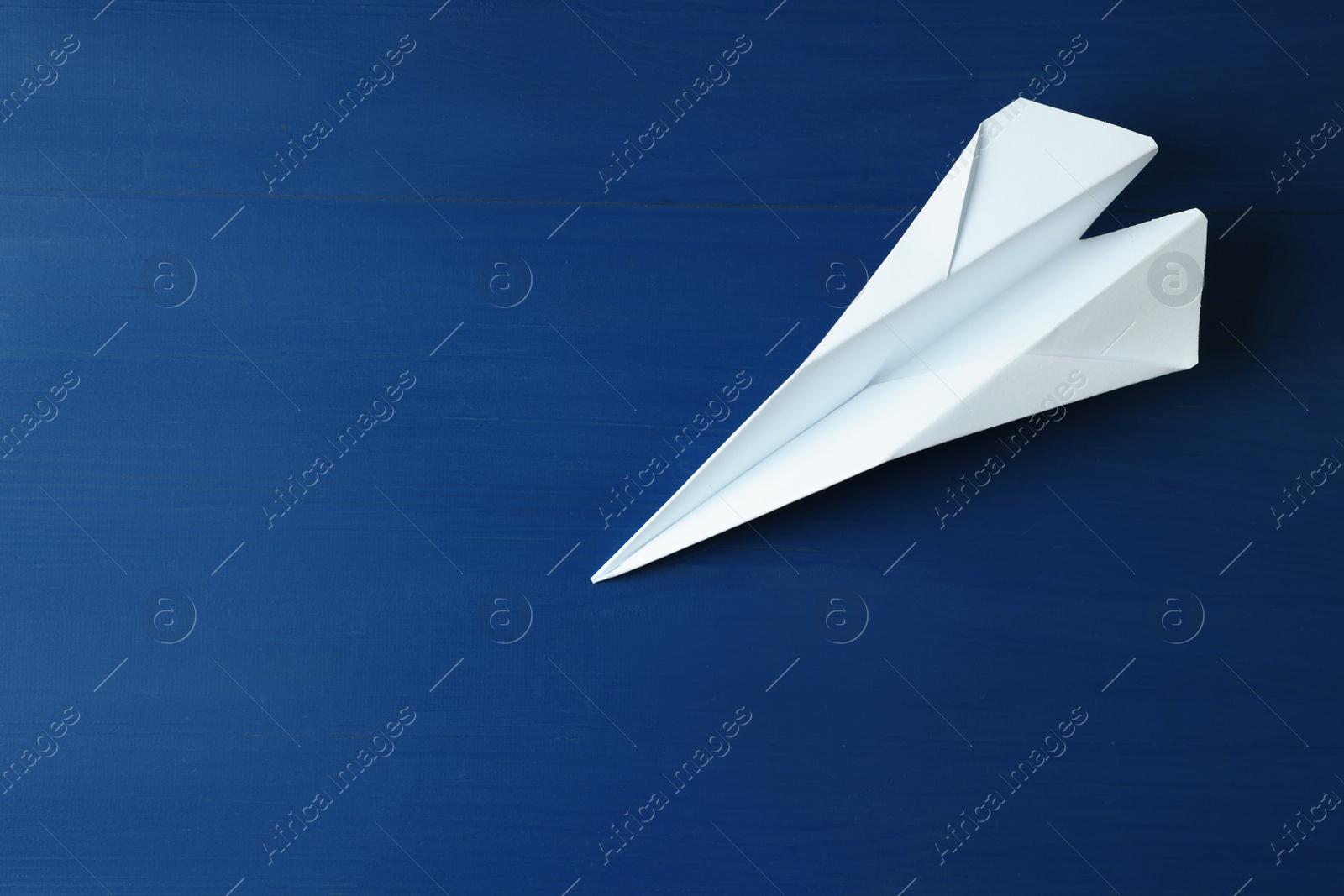 Photo of Handmade paper plane on blue wooden table. Space for text