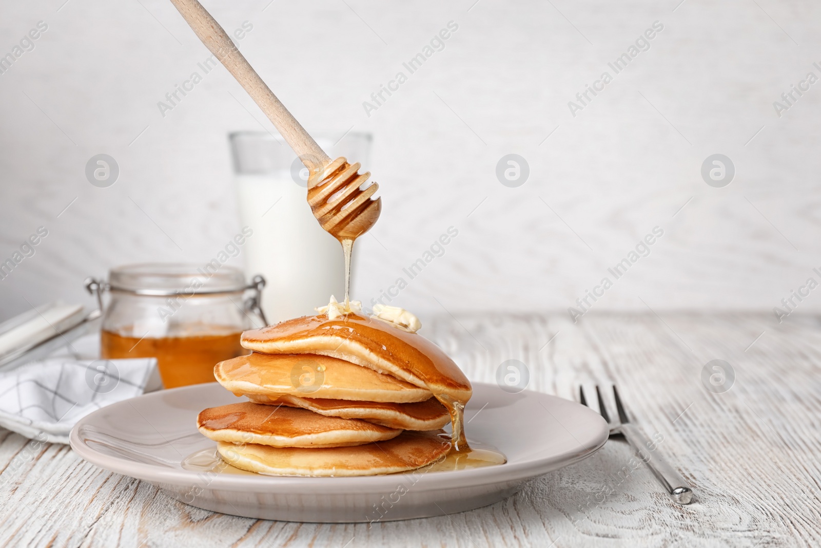 Photo of Pouring honey onto tasty pancakes on table