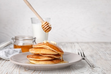 Photo of Pouring honey onto tasty pancakes on table