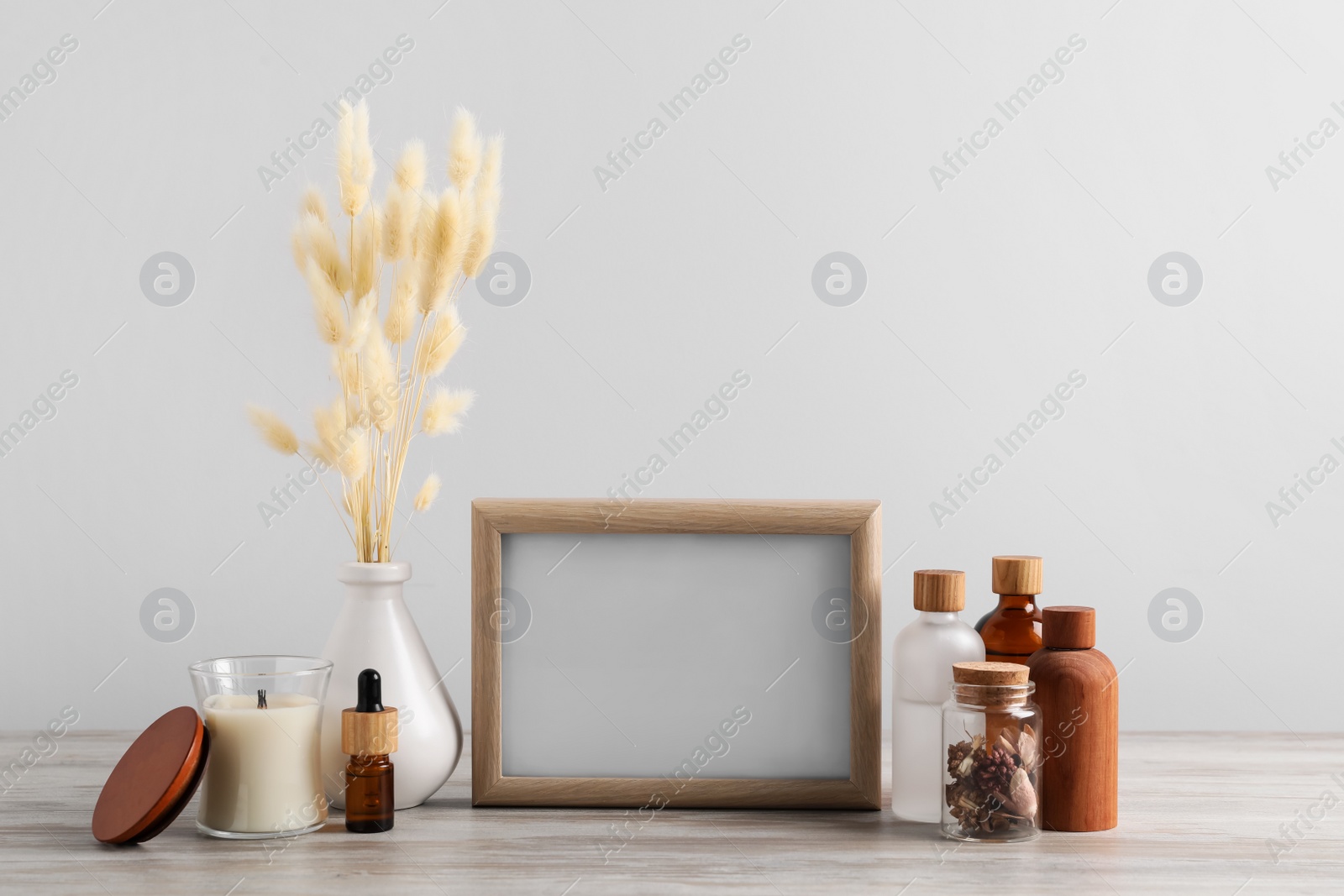 Photo of Blank photo frame, different bottles and decor elements on wooden table