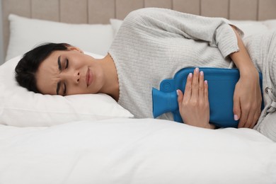 Photo of Woman using hot water bottle to relieve menstrual pain on bed at home